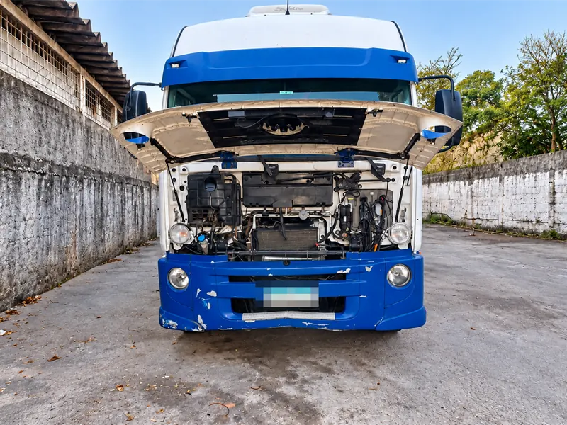 Caminhão com a grade frontal aberta, mostrando o compartimento do motor, em um pátio